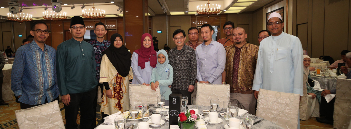 Group of people posed behind a set banquet table, chandeliers and neutral walls in the background.